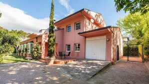 Une maison rose avec un garage, une terrasse avec une table et des chaises, et un grand arbre au premier plan.