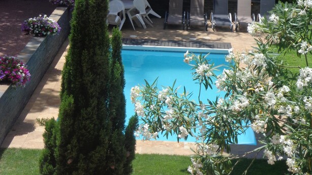 Une piscine entourée d’un jardin avec une pelouse, quelques chaises et une table.