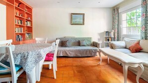 Un salon avec un canapé blanc, une table à manger avec des chaises, une bibliothèque et une fenêtre avec des rideaux.