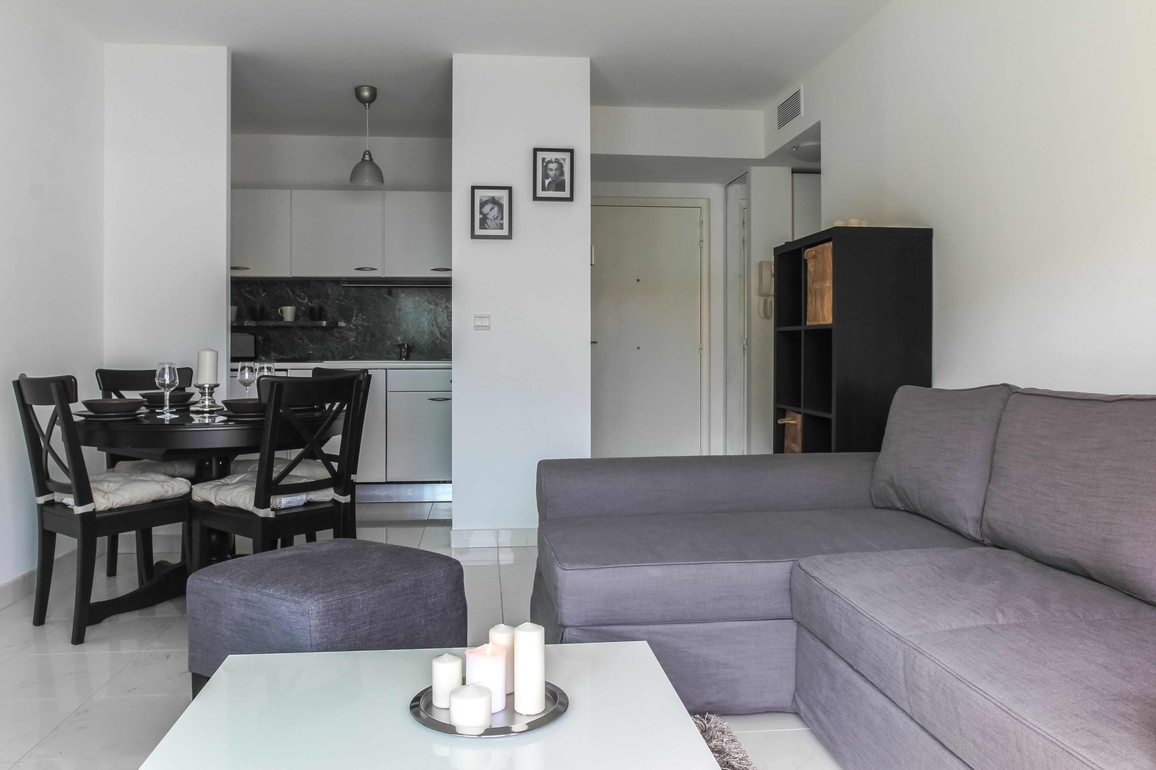 Un salon moderne avec un canapé d’angle gris, une table à manger avec des chaises et une cuisine en arrière-plan.