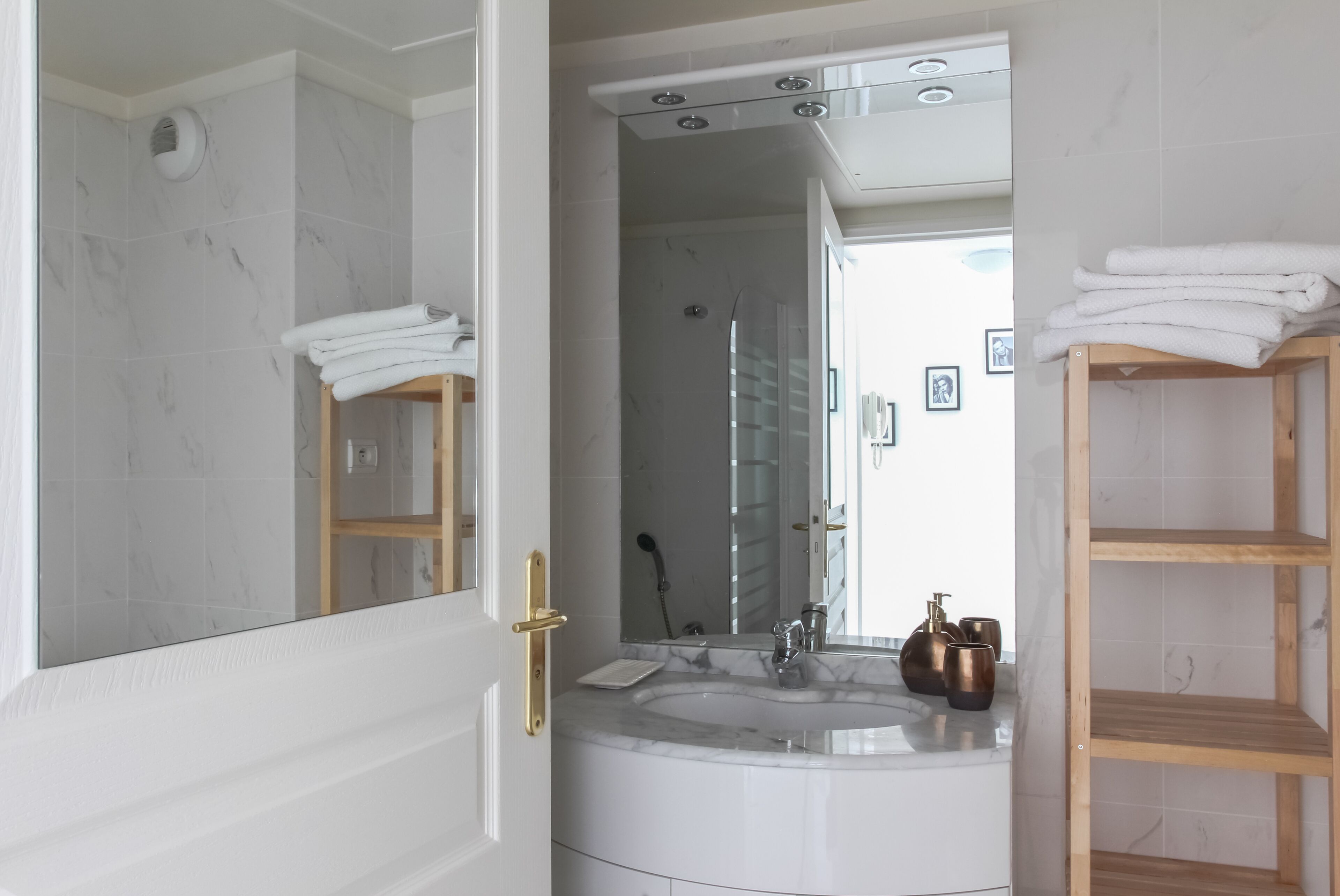 Een badkamer met een marmeren wastafel, een douchecabine met glazen wanden, en een houten plank met handdoeken.
