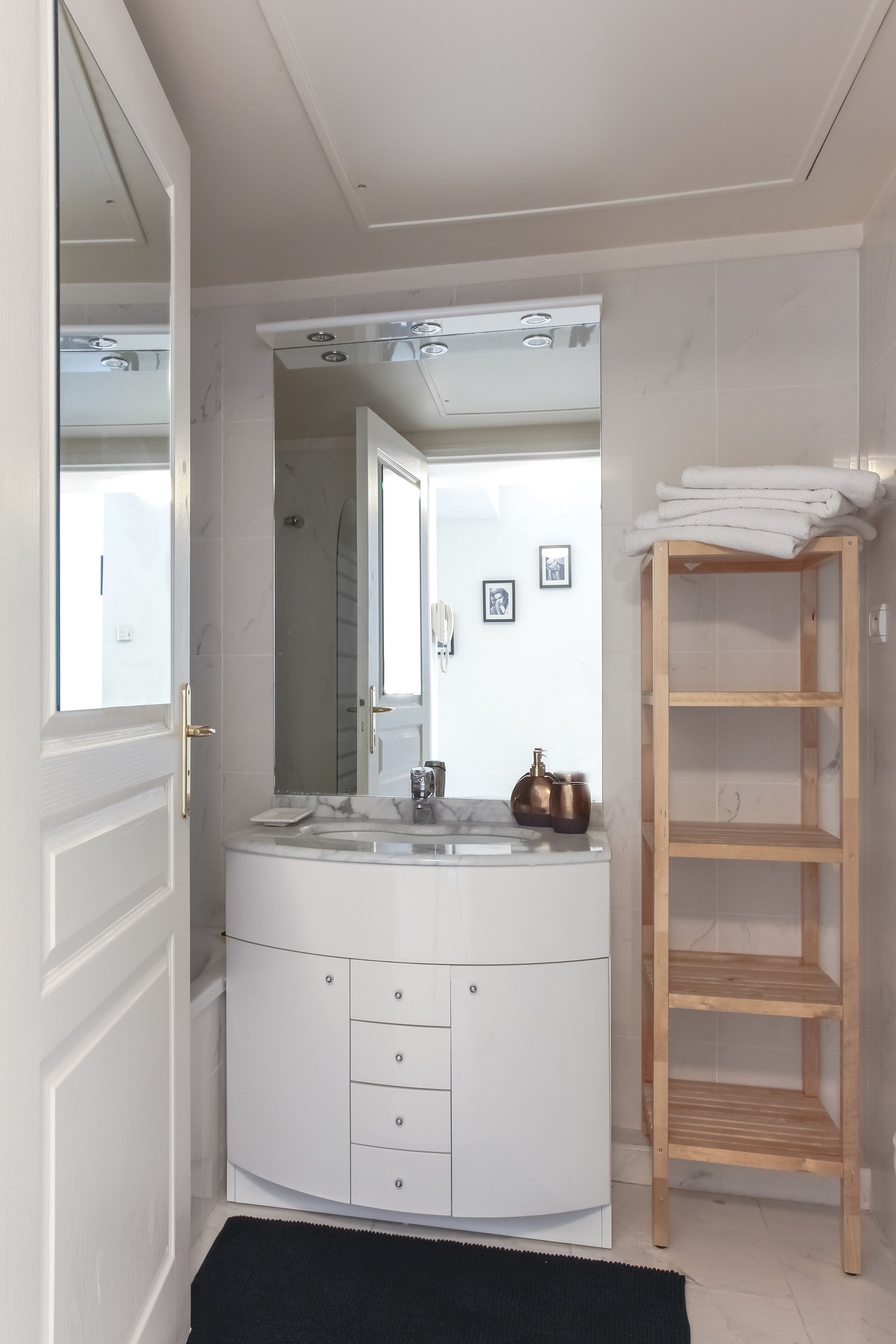 A modern bathroom with a white vanity, a mirror, and a wooden shelf.