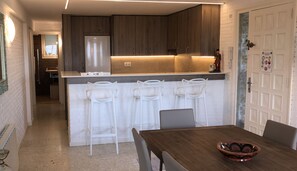 A compact kitchen with wooden cabinets, a stainless steel refrigerator, and a white island with bar stools.