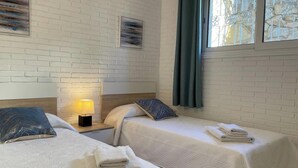 Habitación de hotel con dos camas, ropa de cama blanca, una mesita de noche con lámpara y obras de arte en las paredes.