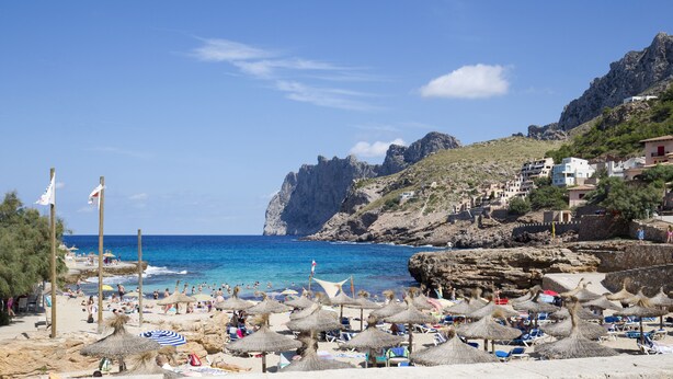 A beach with thatched umbrellas, people sunbathing, and rocky cliffs in the background. - Villa in Uptown Pollensa with spectacular views and private pool (Pollença)