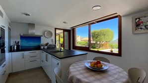 A compact kitchen with a large window, a dining table with a fruit bowl, and a view of greenery outside. - Villa in Uptown Pollensa with spectacular views and private pool (Pollença)
