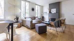Een moderne woonkamer met een bank, een poef en een eethoek met een tafel en stoelen.