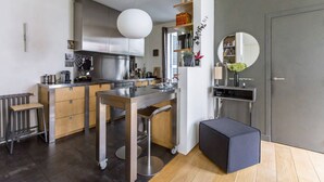 Een moderne keuken met een centraal kookeiland, een eethoek met een bank en een kleine zithoek met een kruk.