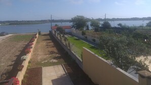 Vistes d'una propietat al costat d'un riu, amb un passeig pavimentat, aigüessos i una zona enjardinada.