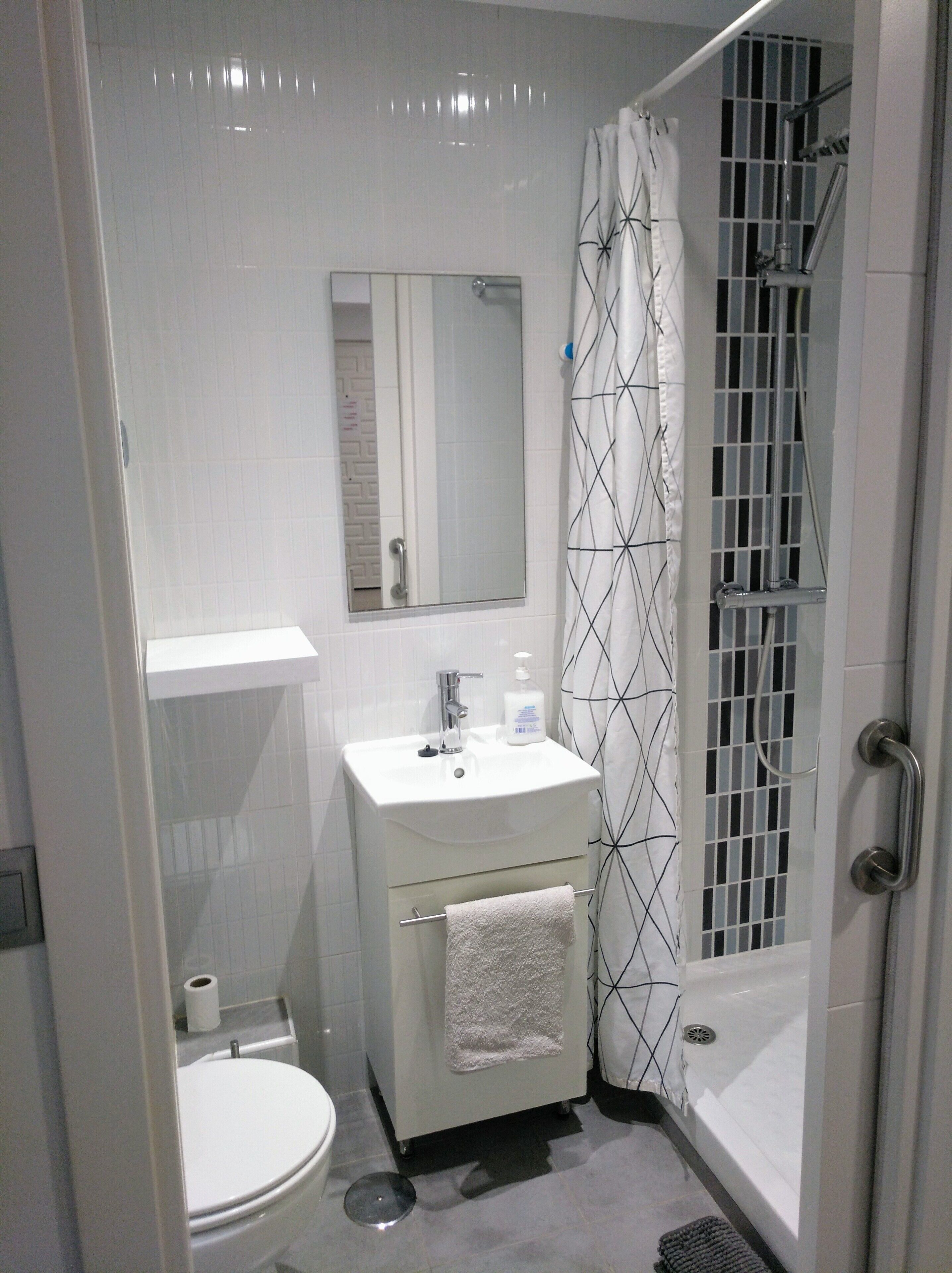 A bathroom with a toilet, sink, mirror, shower, and towel rack.