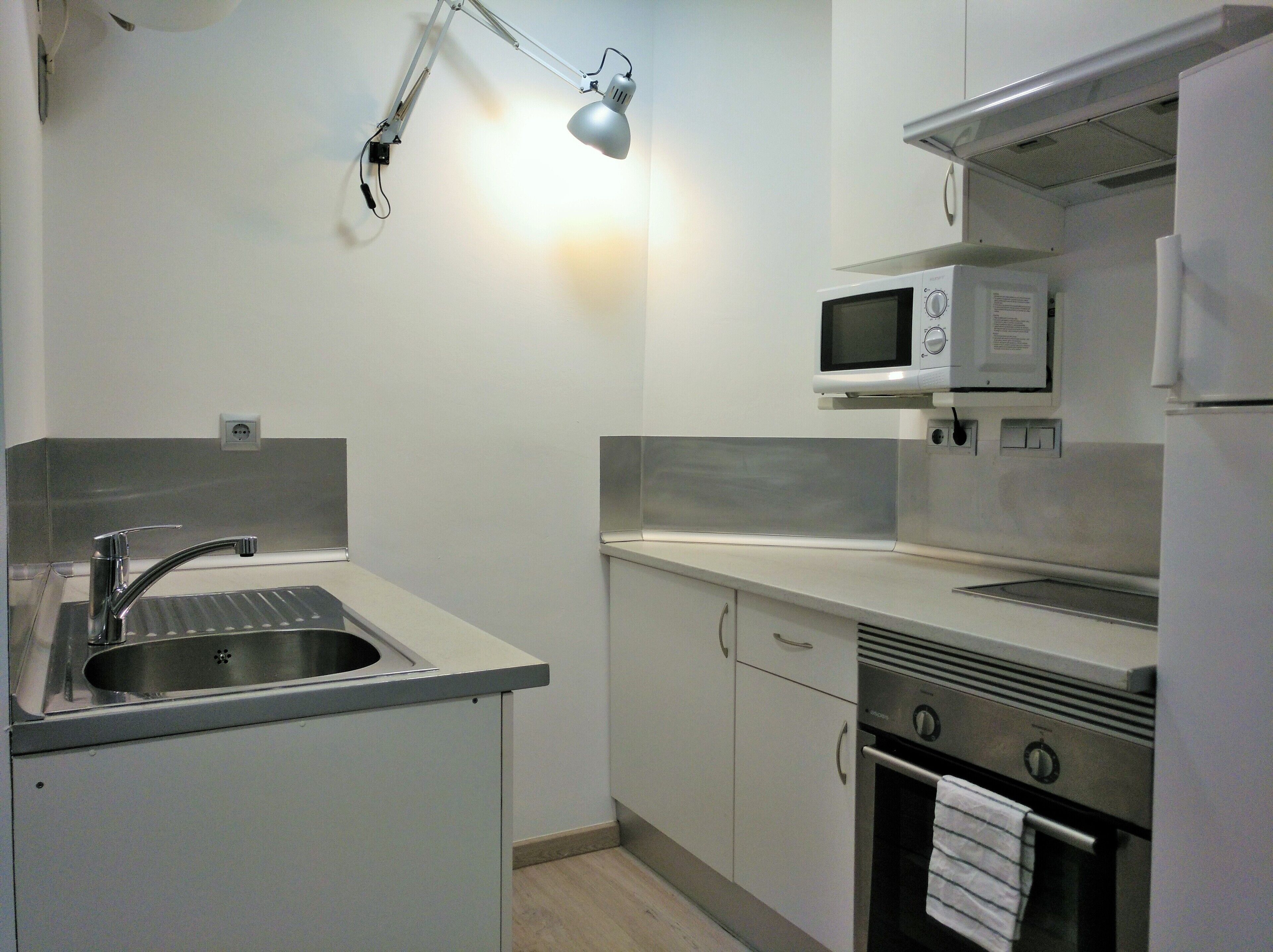 Cocina compacta con pileta, microondas, estufa y un armario.