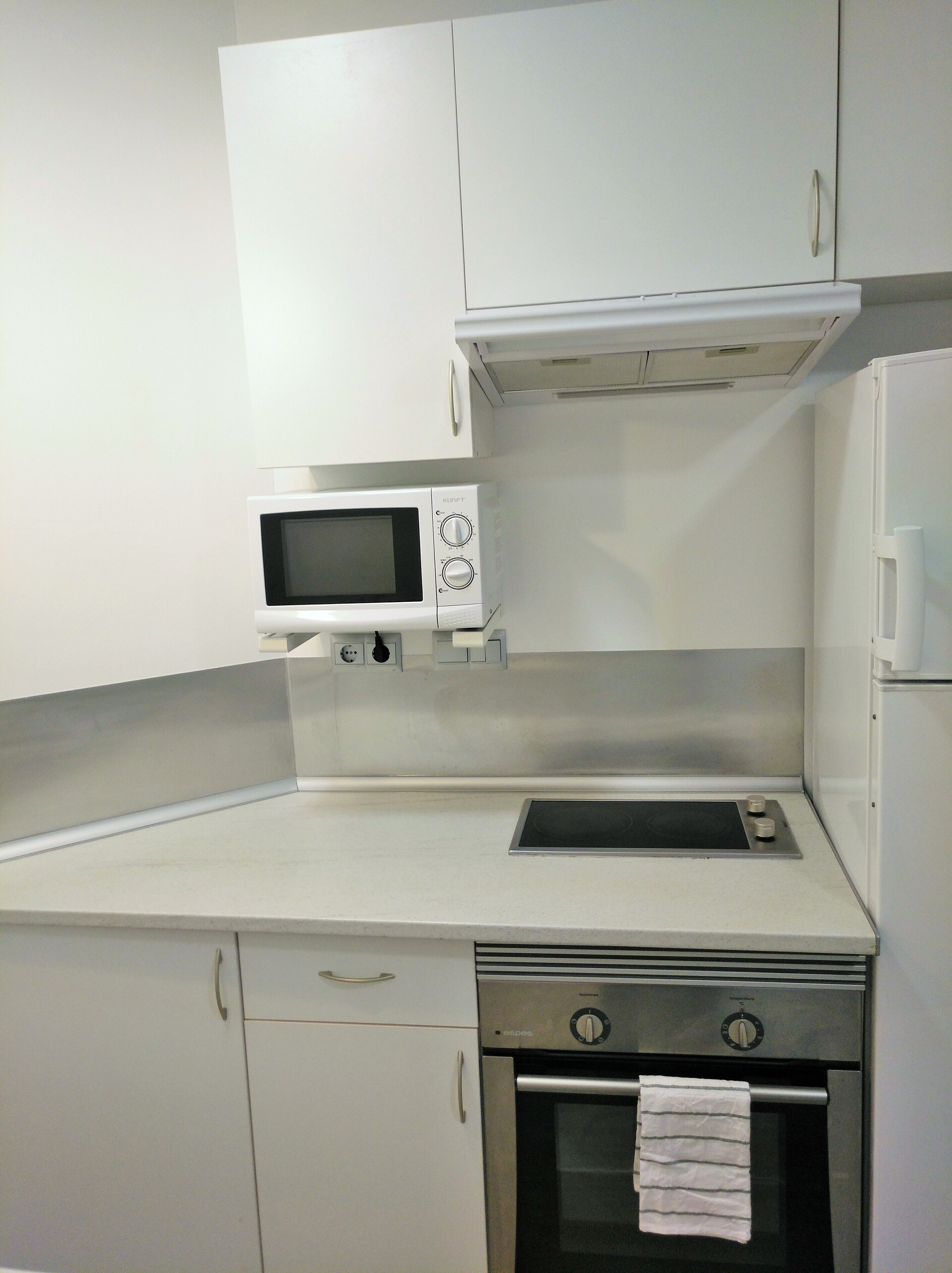 Een compacte keuken met witte kasten, een magnetron, een inbouwoven en een spoelbak.