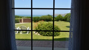 A view through a window with a brick patio, a grassy lawn, and a distant view of the ocean. - Casa Charo with spectacular views of the sea (Cuchía, Miengo)