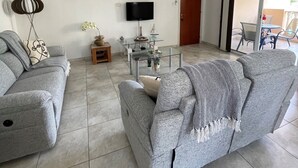 A living room with two grey sofas, a glass coffee table, a ceiling fan, a flat-screen TV, and a painting on the wall. - Luxury apartment, UK TV and free WIFI. Near beach and restaurants, pool view   (Paphos)