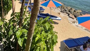 A beach with umbrellas and lounge chairs, a rocky shoreline, and a clear blue sky. - Luxury apartment, UK TV and free WIFI. Near beach and restaurants, pool view   (Paphos)