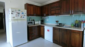 Eine Küche mit Holzschränken, einem weißen Kühlschrank, einer Mikrowelle, einem Geschirrspüler und einer gefliesten Spritzschutzwand.