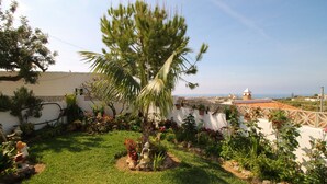 A well-maintained garden with a palm tree, various plants, and a white wall with a decorative fence. - 1003 Villa Cornocalejo (Nerja)