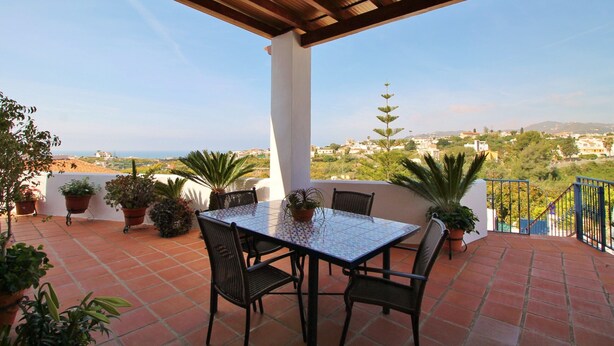 A terrace with a tiled floor, a table with chairs, and potted plants. - 1003 Villa Cornocalejo (Nerja)