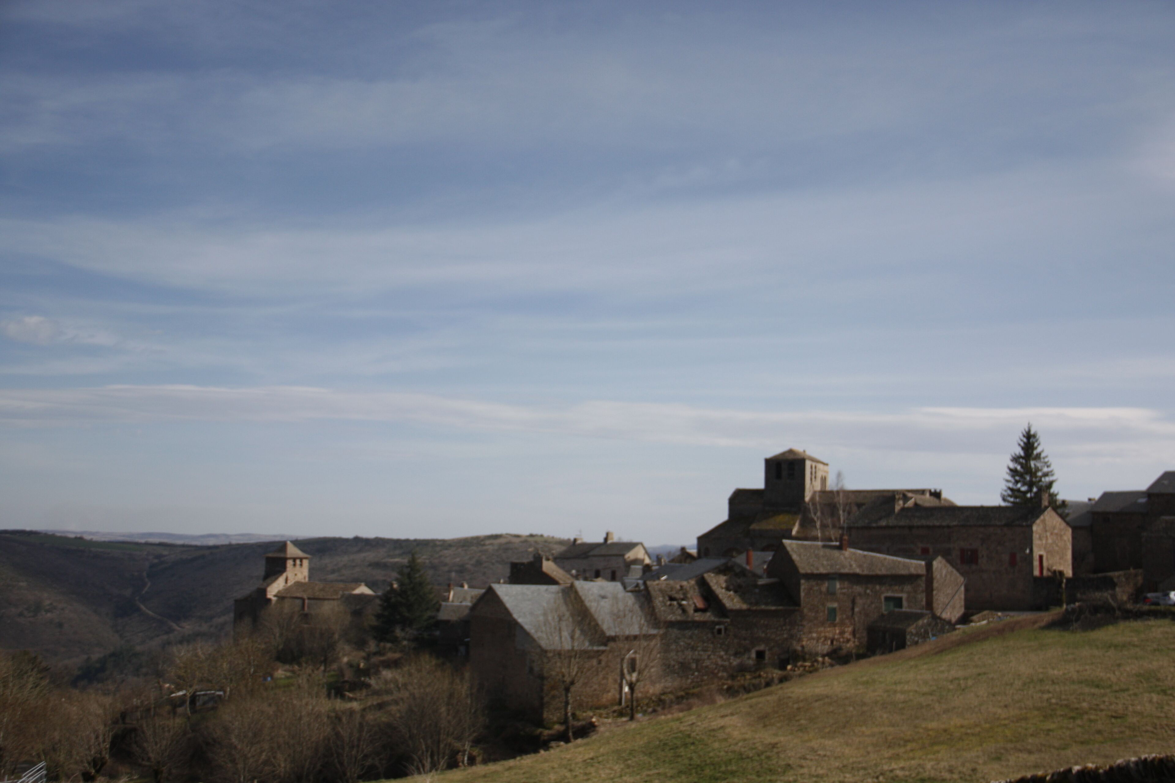 A historic stone building with multiple chimneys, surrounded by a hilly landscape.