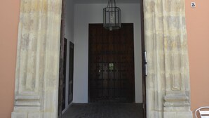 Une entrée en pierre avec un portail en fer forgé, une porte en bois et une chaise en métal sur la droite.
