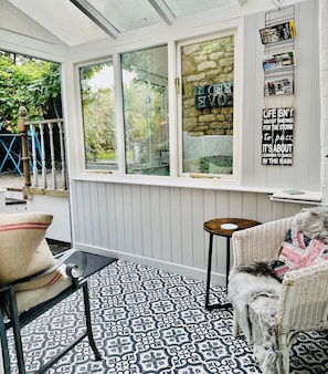 A cozy room with a patterned floor, a wicker chair, a small table, and a dog.