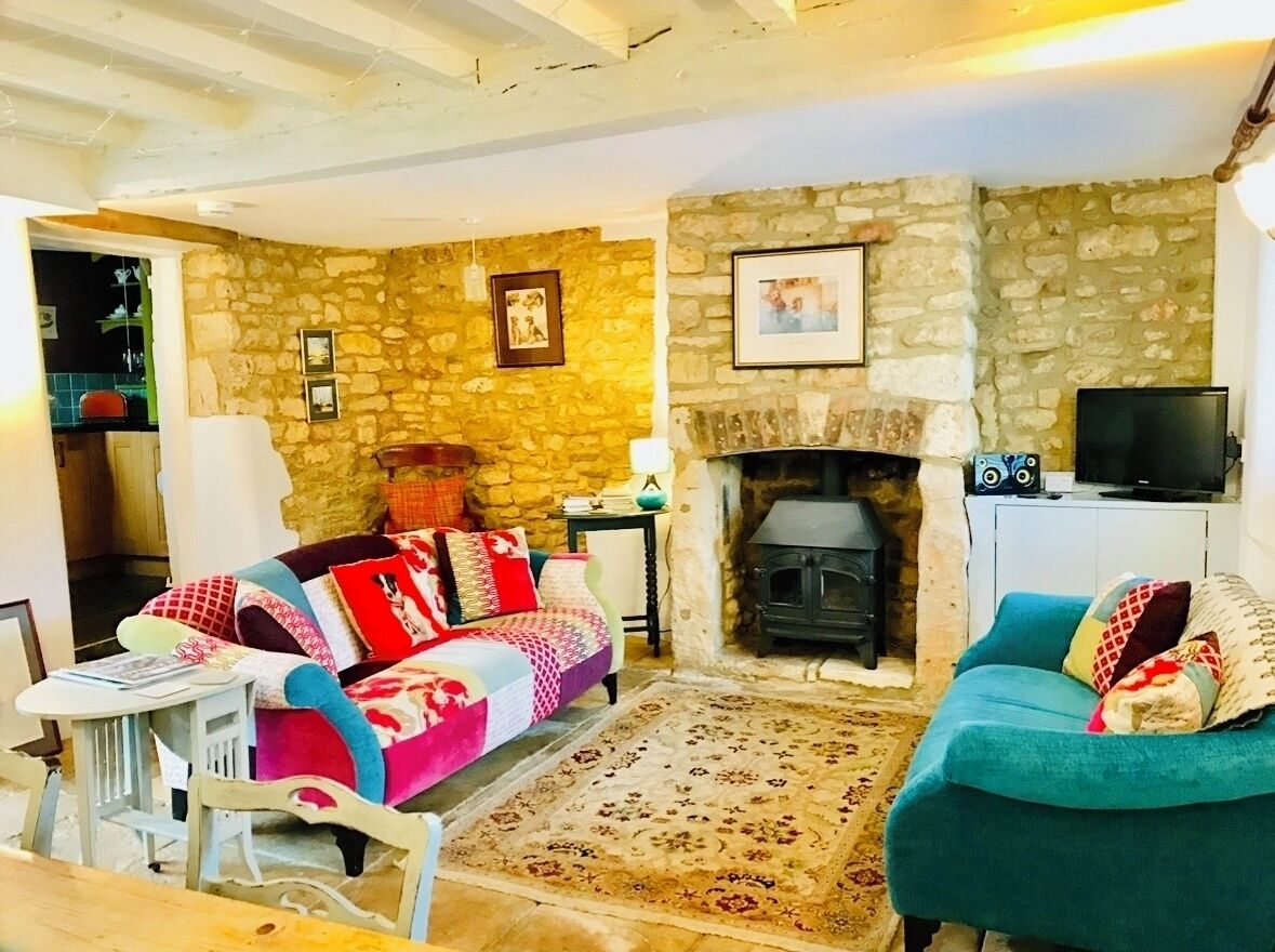 Un salon chaleureux avec un mur en pierre, une cheminée, un canapé, un fauteuil turquoise et un téléviseur.