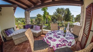 A covered outdoor seating area with wicker furniture, a table with a floral tablecloth, and a view of the surrounding landscape. - A/C 4 bedroom Villa, Pool, sea views beach 6 minutes walk.  Sleeps 8 people. (Pula)