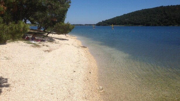 A beach with clear water, a sandy shore, and a forested hill in the background. - A/C 4 bedroom Villa, Pool, sea views beach 6 minutes walk.  Sleeps 8 people. (Pula)