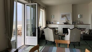 A room with a large sliding glass door leading to a balcony, a fireplace, a dining table with chairs, and a sofa. - Beautiful 4* villa on the sand, feet in the water, stunning bay views (Le Crotoy)