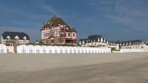 A coastal building with a prominent tower, adjacent beach huts, and a sandy beach. - Beautiful 4* villa on the sand, feet in the water, stunning bay views (Le Crotoy)