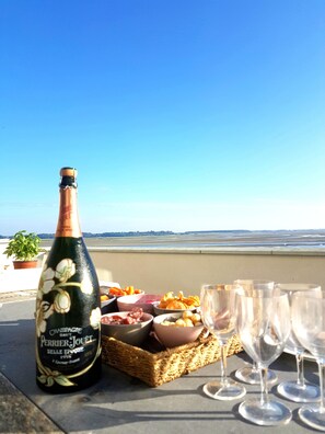 A bottle of champagne, a basket of snacks, and empty glasses on a table with a view of the beach.