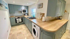 A compact kitchen with grey cabinets, a built-in microwave, a washing machine, and a wooden countertop. - Cosy Character Cottage With Sea View In Mousehole (Mousehole, Penzance)