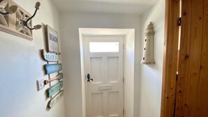 A narrow hallway with a white door, wooden floor, and a wall with various signs. - Cosy Character Cottage With Sea View In Mousehole (Mousehole, Penzance)