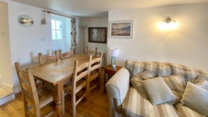 A cozy living room with a wooden dining table and chairs, a striped sofa, a lamp, and a framed picture on the wall. - Cosy Character Cottage With Sea View In Mousehole (Mousehole, Penzance)