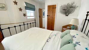 A bedroom with a bed, a window with a blue blind, a wooden door, and a wall-mounted plant. - Cosy Character Cottage With Sea View In Mousehole (Mousehole, Penzance)