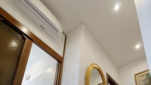 Un couloir doté d’un plancher en bois, d’une armoire en bois avec une façade à treillis, d’un grand miroir ovale et d’un climatiseur fixé au mur.