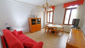 Un salon avec un canapé rouge, une table à manger en bois et des chaises. On y trouve un meuble avec des portes en verre et un téléviseur posé sur un meuble en bois.