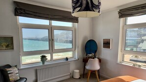 Une chambre avec une grande fenêtre, un lit, une chaise, une commode et un miroir.