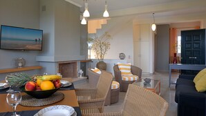Ein modernes Wohnzimmer mit Rattanmöbeln, einem Esstisch mit Obst und einem Kamin.