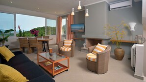 Ein modernes Wohnzimmer mit einer Couch, Sesseln, einem Couchtisch, einem Fernseher und einem Kamin.