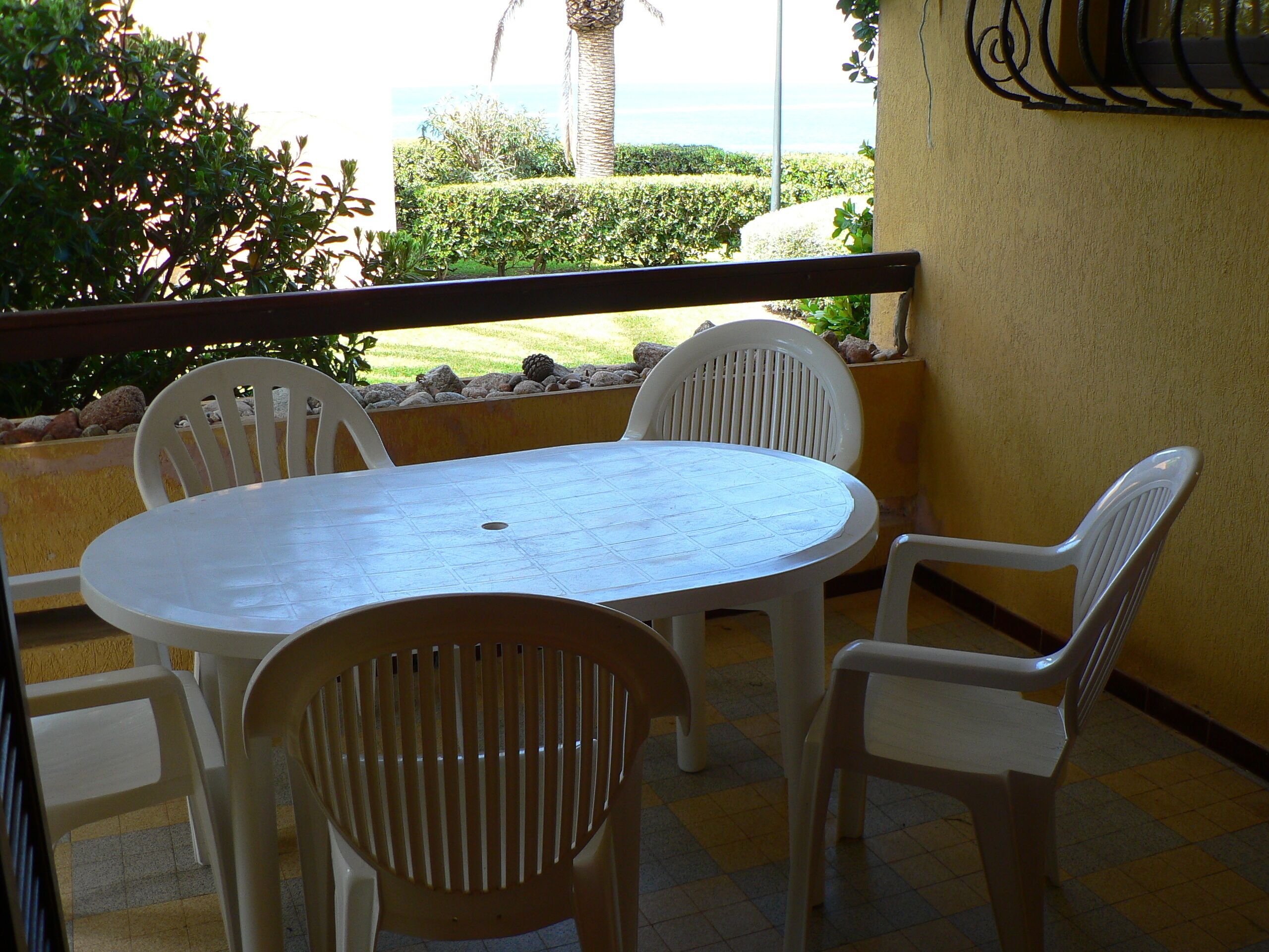 Une terrasse avec une table ronde et quatre chaises, donnant sur un jardin aménagé et l’océan.