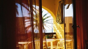 Visão pela janela com moldura de madeira, uma cadeira branca e uma mesa em primeiro plano.