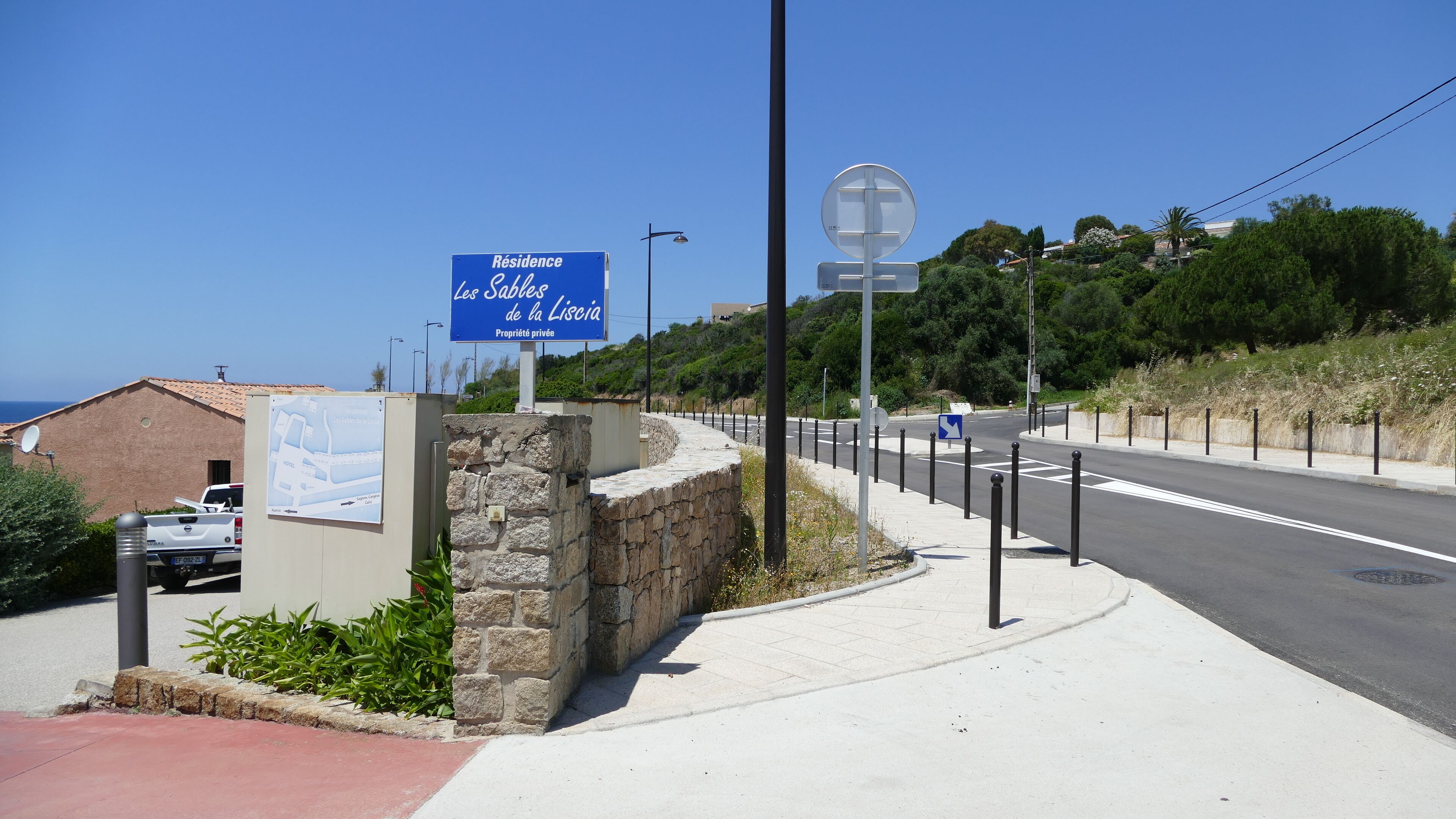 A sign for a private residence named 'Résidence Les Sabbes de la Licérie' with a stone wall and a paved sidewalk.