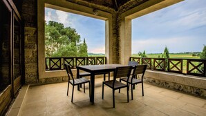 Um alpendre coberto com mesa e cadeiras, chão de pedra e vista para o campo.