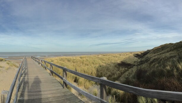 Un paseo marítimo que lleva a una playa con dunas y un cielo despejado.
