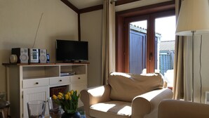 Una sala de estar con sofá, televisor, mesa de centro con vasos y un florero, y ventana con cortinas.