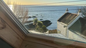 Uitzicht vanuit een raam op een wateroppervlak met land in de verte, een heldere lucht en een houten constructie met een schuin dak.