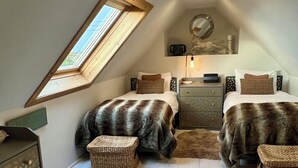 Een gezellig slaapkamer op zolder met twee bedden, een dakraam, een klein bureau en een spiegel.