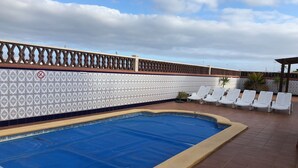 Una piscina con un muro piastrellato, lettini prendisole e un pergolato.