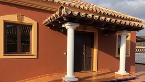 Un edificio con tetto in tegole, un ingresso coperto con colonne bianche e una finestra con cornice decorativa.